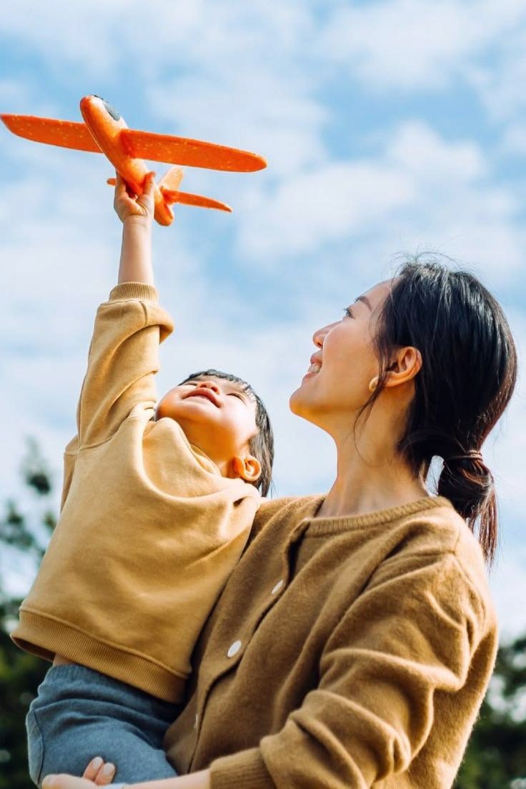 Ibu dan anak bermain pesawat mainan di bawah langit cerah